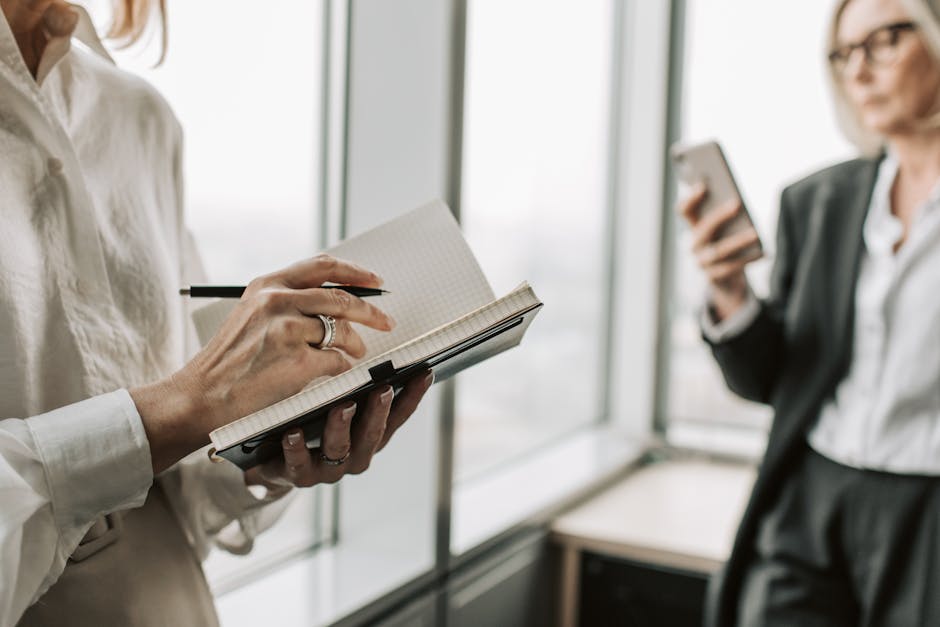 Businesswomen collaborating in an office setting, writing notes and using a smartphone.